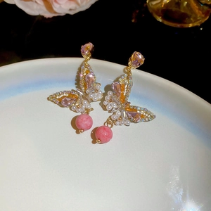 Détail des boucles d'oreilles papillon dorées avec cristaux roses et perles