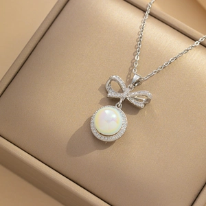 Silver bow necklace with a shimmering pearl pendant in a textured jewelry box