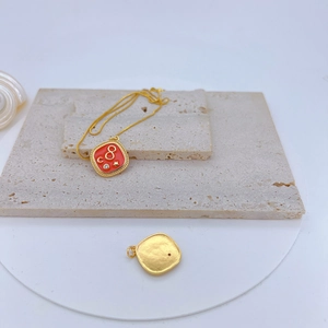Macro detail of gold-plated necklace with red enamel square pendant on stone
