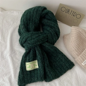 Detail of dark green Shetland Virgin Wool scarf with stitched logo label on white fabric