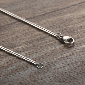 Close-up of silver stainless steel curb chain with secure lobster clasp on wood
