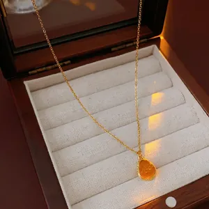 Gold plated necklace with amber teardrop pendant displayed in a vintage wooden jewelry box