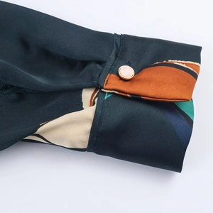 Detailed close-up of dark green printed shirt cuff with silk texture and metal-rimmed button