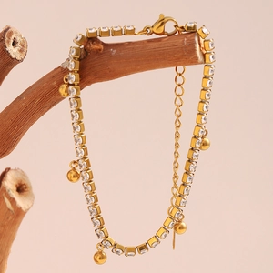 Detail of 18K gold plated bracelet with square zircons and round bead charms on branch
