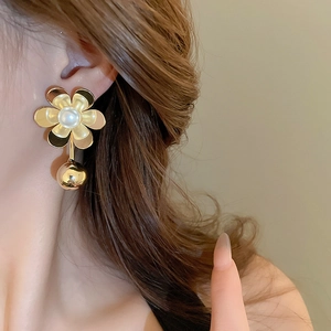 Detail of gold floral earrings with pearls and bead pendants worn by a model