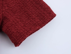 Close-up of red tweed dress fabric showing detailed woven texture and sleeve cuff finish
