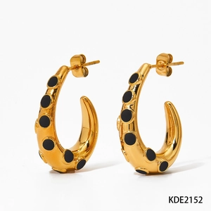Macro detail of golden C-shaped oval earrings with black dotted enamel pattern
