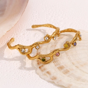 Detail of 18K gold branch-textured bracelets with colorful inlaid gemstones on a shell