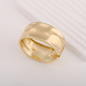 Detail of a wide gold metal cuff with a unique hammered texture and hinge closure