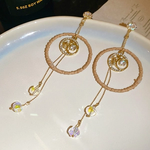 Detail of tassel earrings with woven ring, moon charm and iridescent crystals on tray