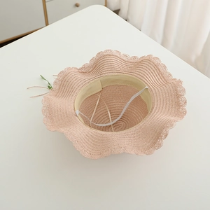 Detailed view of pink woven straw hat with wavy brim, interior sweatband and wind rope