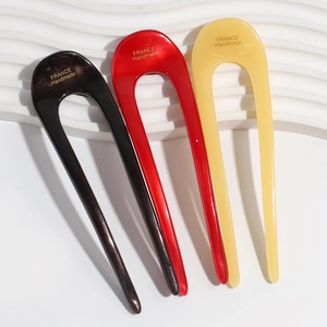 Chic U-shaped acetate hair pins in black, red, and beige on a white wavy background