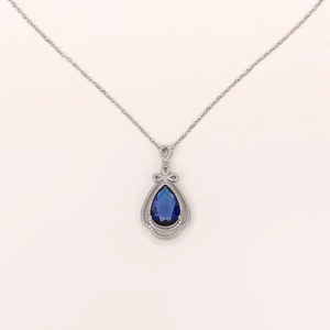 Macro view of blue pear-cut sapphire pendant with pavé halo and bow detail