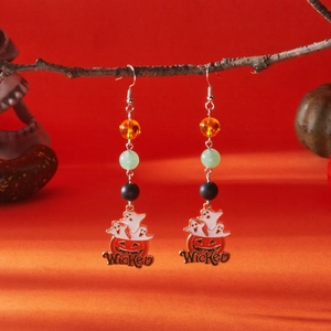 Detail of Halloween drop earrings with 'Wicked' charm and colorful beads on a branch