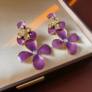 Detail of purple enamel flower earrings with gold petals and crystal center on a jewelry box