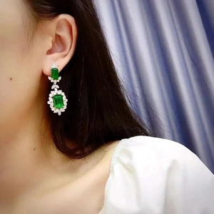 Macro view of emerald-style drop earrings with green rectangular stones and diamonds
