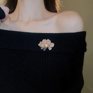 Close-up of pink flower brooch with gold edges and pearl on a black knit sweater