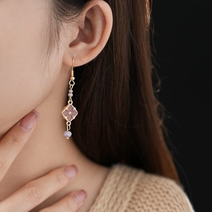 Detail of vintage gold drop earring with purple beads and flower pendant on model