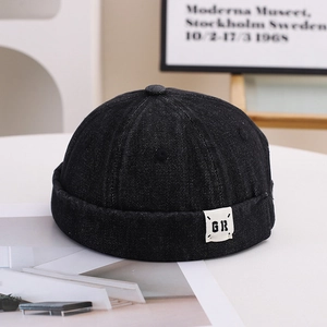 Detail of a black cotton docker hat with side woven label on a minimalist white table