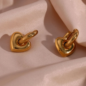 Macro shot of polished gold-plated heart pendant earrings on pink silk fabric background