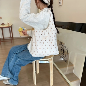 Quilted canvas shoulder bag with brown bear print worn by model in a cozy cafe setting