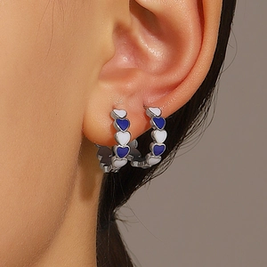 Close-up of silver C-shaped heart earrings with blue and white enamel inlay