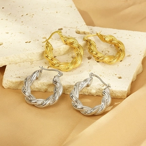 U-shaped twisted hoop earrings in gold and silver finish on natural stone background