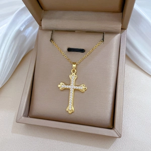 Close-up of gold-plated cross necklace with sparkling crystals in a beige jewelry box