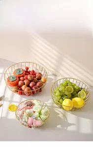 Close-up of golden geometric metal wire fruit basket on marble surface with natural shadows