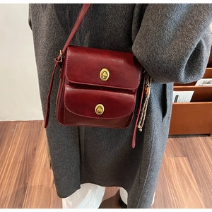 Model wearing a vintage dark red PU leather crossbody bag with dual gold buckles and tassels
