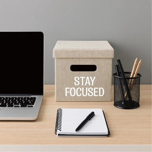Beige fabric storage box with Stay Focused print on a desk with office supplies