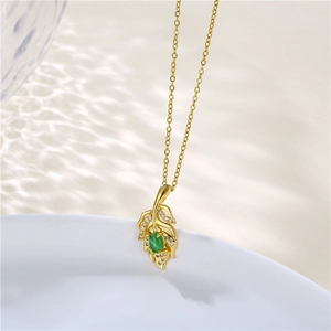 Detail shot of golden leaf pendant with green gemstone and zircon stones on a fine chain
