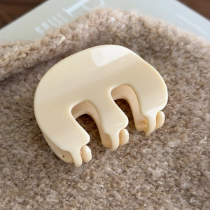 Detailed view of a cream acrylic M-shaped claw clip on soft textured fabric