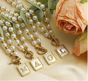 Detailed shot of gold OT buckle pearl necklaces with square shell initial pendants