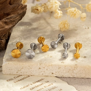 Titanium sun-shaped labret studs in gold and silver finish on a rustic stone background