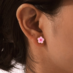 Close-up of a pink flower stud earring with gold edges worn on a woman's earlobe