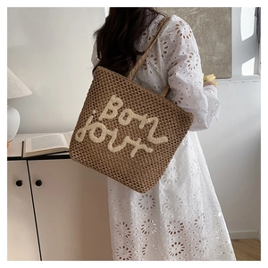 Detail of hand-woven straw tote bag with plush 'Bon jour' embroidery for summer beach vacation