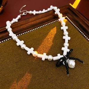 Detailed view of artificial pearl necklace with cross beads and black bow pendant