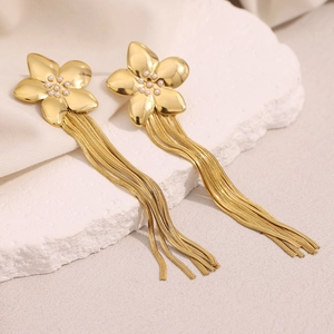 Detail view of 18K gold plated flower earrings with long tassels on a white stone pedestal