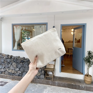 Close-up of white corduroy makeup bag held in hand featuring vertical ribbed texture