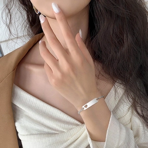 Detail of silver bar bracelet featuring a heart cutout and delicate woven chain texture