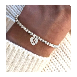 Silver bead bracelet with a heart pendant featuring letter R on a woman wrist