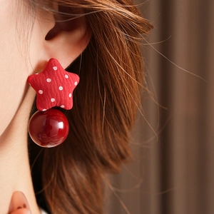 Close-up of red polka dot star earrings with pearl detail worn by a model