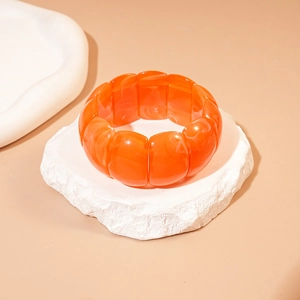 Macro shot of orange geometric acrylic bead bracelet on a textured stone base