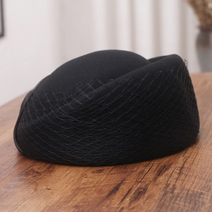 Detail of vintage black wool pillbox hat featuring delicate mesh veil on a wooden desk
