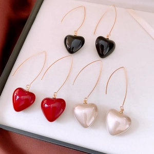 Détail de trois boucles d'oreilles pendantes en forme de cœur, noir, rouge et blanc