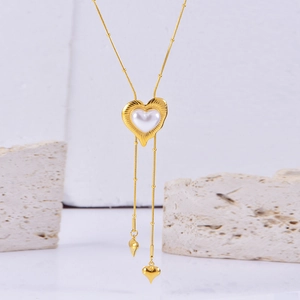 Macro detail of gold heart pendant with pearl inlay on long Y-shaped snake bone tassel chain