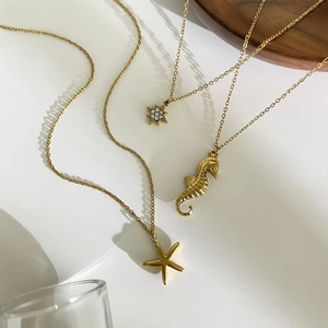 Colliers dorés avec pendentifs étoile de mer et hippocampe sur plateau en bois