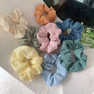 Detailed view of textured bubble fabric scrunchies in various pastel colors on a stone surface