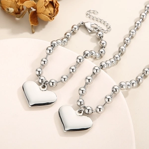 Detail of silver beaded jewelry set with heart pendants on a white tray with dried flowers